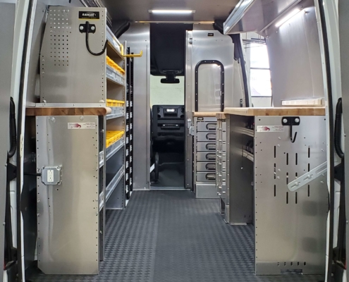 A van upfit with shelves and a workstation from an outside rear view